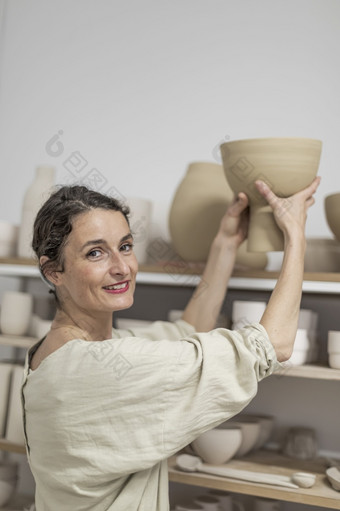 女陶艺家在室内持有手工制作的粘土产品概念陶器