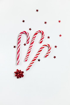 圣诞节作文三个焦糖糖果拐杖五彩纸屑星星和红色的弓白色背景节日最小的风格平躺为问候卡邀请社会媒体垂直