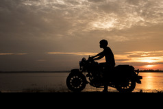 轮廓男人。骑电动机自行车与日落旅行概念