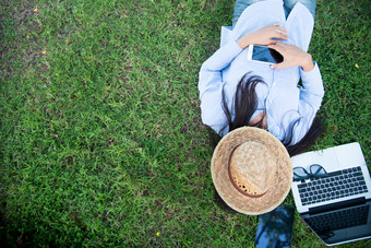聪明的女人工作户外自由使用移动PC聪明的平板电脑和聪明的电话躺下来绿色草场阅读电子表格工作从首页业务概念