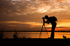 轮廓英俊的摄影师取照片与专业相机的日落