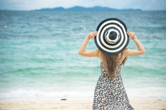 夏天时间如此女人假期的海滩快乐的女人穿夏天衣服和稻草帽子坐着的海滩看海时间放松夏天生活方式户外拍摄热带岛海滩