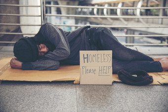 无家可归的人人贫困乞丐男人。问为钱工作和希望帮助无助的脏城市坐着与标志纸板盒子说无家可归的人请帮助董事会乞丐城市概念