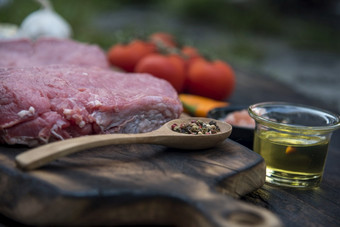 前视图生牛肉肉牛排成分未煮过的厨房木董事会牛排西方厨房成分<strong>新鲜</strong>的肉胡椒橄榄石油大蒜辣椒<strong>番茄</strong>盐和迷迭香户外为聚会，派对西方食物概念