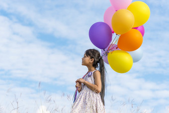 快乐的可爱的女孩持有气球运行绿色草地白色云和蓝色的天空与幸福手持有充满活力的空气气球玩生日聚会，派对快乐次夏天阳光户外