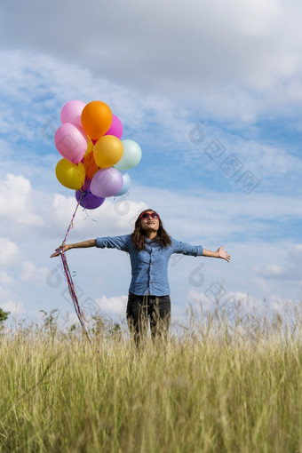 女人持有气球运行绿色草地白色云和蓝色的天空与幸福快乐的和放松手持有充满活力的空气气球玩生日聚会，派对快乐次夏天阳光户外