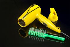 黄色的可折叠的电手持头发干燥机为头发沙龙理发师商店的黑色的镜子背景与绿色梳子黄色的可折叠的头发干燥机的黑色的镜子背景