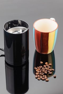 黑色的咖啡磨床与一些咖啡豆子和杯子的灰色镜子背景咖啡磨床与咖啡豆子和杯子的灰色镜子背景