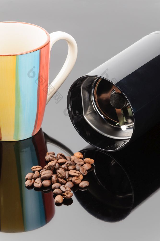 黑色的咖啡磨床与一些咖啡豆子和杯子的灰色镜子背景咖啡磨床与咖啡豆子和杯子的灰色镜子背景