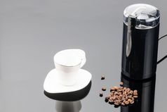 黑色的咖啡磨床与一些咖啡豆子和杯的灰色镜子背景复制空间咖啡磨床与咖啡豆子和杯的灰色镜子背景复制空间