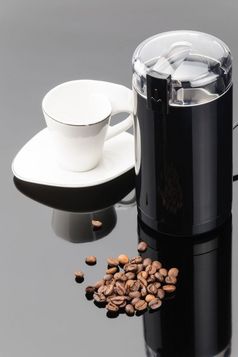 黑色的咖啡磨床与一些咖啡豆子和杯的灰色镜子背景咖啡磨床与咖啡豆子和杯的灰色镜子背景