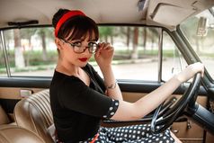 肖像高加索人美丽的年轻的女孩黑色的古董衣服和古董眼镜摆姿势后面的轮古董车