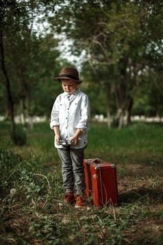 高加索人小男孩古董衣服的公园与老手提箱和复古的相机他的手