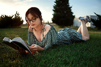 年轻的高加索人女孩古董复古的衣服读取书的草坪上在日落
