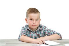 高加索人学龄男孩格子衬衫坐着的表格和写作一块纸在那里也移动PC和电话的表格