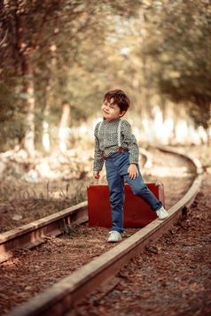 小可爱的男孩古董衣服站被遗弃的铁路与古董手提箱他的手