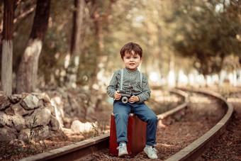 小可爱的男孩古董衣服站被遗弃的铁路与古董手提箱与<strong>老相机</strong>他的手