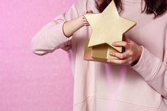 礼物盒子的形状黄金明星的手年轻的亚洲女孩粉红色的孤立的背景