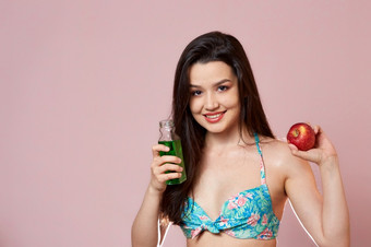年轻的美丽的纤细的亚洲女孩泳衣与新鲜的汁和苹果他的手微笑粉红色的孤立的背景