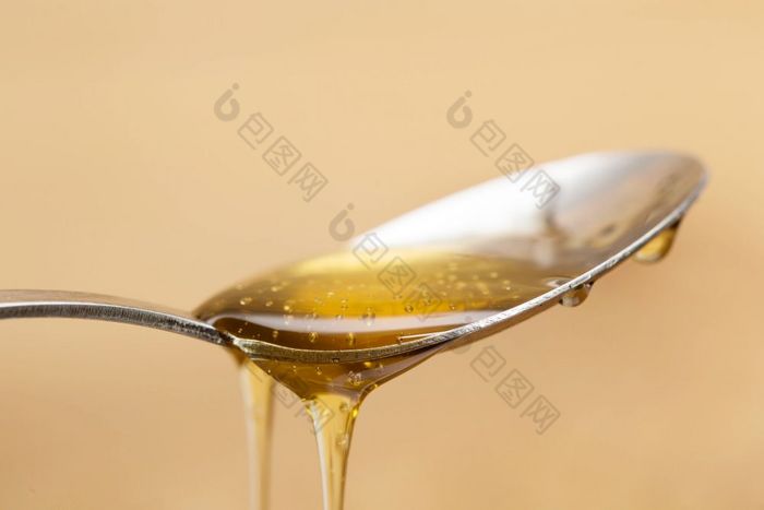 闪亮的金蜂蜜滴从银勺子与木棕色（的）背景甜蜜的闪亮的金蜂蜜滴从银勺子与木棕色（的）背景