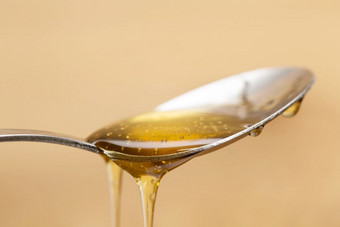 闪亮的金蜂蜜滴从银<strong>勺子</strong>与木棕色（的）背景甜蜜的闪亮的金蜂蜜滴从银<strong>勺子</strong>与木棕色（的）背景