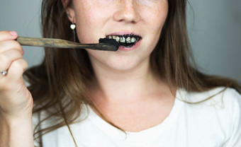 年轻的女人刷牙她的牙齿与黑色的牙粘贴与活跃的木炭和黑色的牙刷白色背景为牙齿美白清洁年轻的女人刷牙她的牙齿与黑色的牙粘贴与活跃的木炭和黑色的牙刷白色背景为牙齿美白