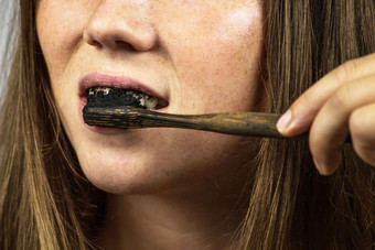 年轻的女人刷牙她的牙齿与黑色的牙粘贴与活跃的木炭和黑色的牙刷白色背景为牙齿美白清洁年轻的女人刷牙她的牙齿与黑色的牙粘贴与活跃的木炭和黑色的牙刷白色背景为牙齿美白