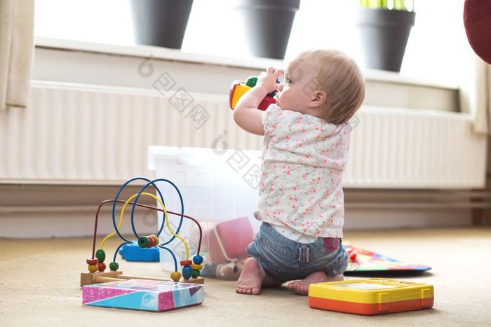 婴儿玩独自一人与玩具地毯的地板上首页混乱的婴儿玩独自一人与玩具地毯的地板上首页