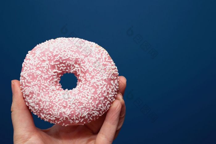 手持有美味的色彩斑斓的甜甜圈与洒附近黑暗蓝色的背景糖概念手持有美味的色彩斑斓的粉红色的甜甜圈与洒附近黑暗蓝色的背景糖概念
