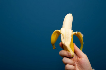 去皮黄色的香蕉水果附近蓝色的背景手健康的概念特写镜头去皮黄色的香蕉水果附近蓝色的背景手健康的概念