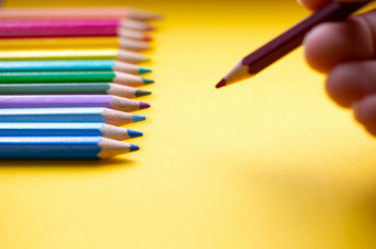 彩色的铅笔行彩虹颜色手与蓝色的彩色的铅笔吸引了橙色纸复古的背景空间为文本彩色的铅笔行彩虹颜色手与蓝色的彩色的铅笔吸引了橙色纸复古的背景