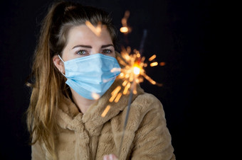 快乐新一年肖像年轻的女人穿医疗面具和持有罗马焰火筒光的黑暗为新冠病毒冠状病毒和新一年概念特写镜头快乐新一年肖像年轻的女人穿医疗面具和持有罗马焰火筒光的黑暗为新冠病毒冠状病毒和新一年概念