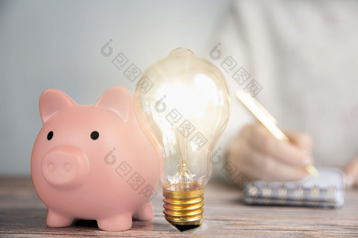 闪亮的灯泡和粉红色的小猪银行业务人写作金融的想法有创意的储蓄投资预算概念复制空间特写镜头闪亮的灯泡和粉红色的小猪银行业务人写作金融的想法有创意的储蓄投资预算概念复制空间