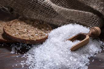 白色海盐为烹饪食物解雇了木表格自然勺子面包和粗袋白色海盐为烹饪食物黑暗木表格自然勺子面包和粗袋