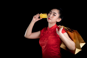 肖像美丽的年轻的亚洲女人红色的衣服传统的旗袍持有信贷卡和购物袋的黑色的背景中国女孩中国人新一年概念看的相机