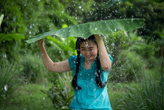 肖像年轻的亚洲女人与黑色的头发持有香蕉叶的下雨的绿色花园背景