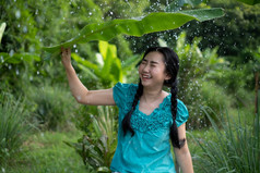 肖像年轻的亚洲女人与黑色的头发持有香蕉叶的下雨的绿色花园背景