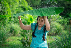 肖像年轻的亚洲女人与黑色的头发持有香蕉叶的下雨的绿色花园背景