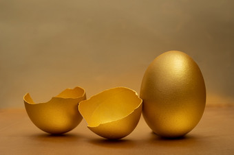 金蛋和一半破碎的鸡蛋与蛋黄的金背景