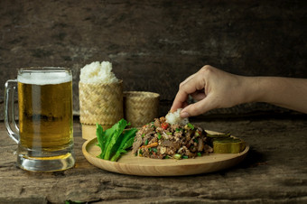 使用手吃黏糊糊的大米和辣的剁碎猪肉沙拉与啤酒拉布传统的泰国食物的文化的人的东北泰国