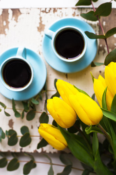 两个蓝色的杯咖啡与黄色的郁金香老表格前视图新鲜酿造咖啡
