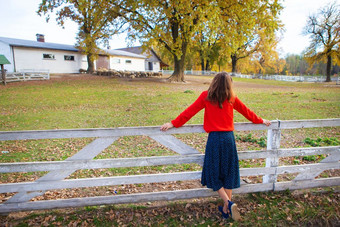 美丽的女孩红色的毛衣站与她的回来附近白色木栅栏美丽的秋天美丽的女孩红色的毛衣站与她的回来附近白色木栅栏美丽的秋天