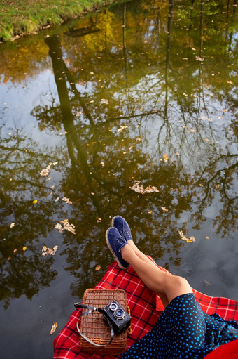 的腿小女孩附近的湖谎言红色的格子格子美丽的反射的水下降叶子的水视图从以上腿年轻的女孩附近的湖格子红色的笼子里美丽的反射的水视图从以上