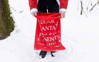 男人。穿着圣诞老人老人持有大红色的袋与礼物为孩子们男人。穿着圣诞老人老人持有大红色的袋与礼物为孩子们