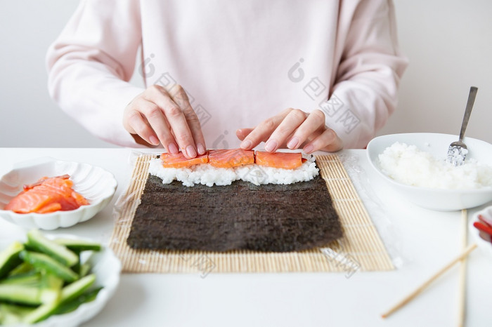 寿司准备过程的女孩使寿司与不同的口味新鲜的大马哈鱼鱼子酱鳄梨黄瓜姜大米寿司准备过程的女孩使寿司与不同的口味新鲜的大马哈鱼鱼子酱鳄梨黄瓜姜大米