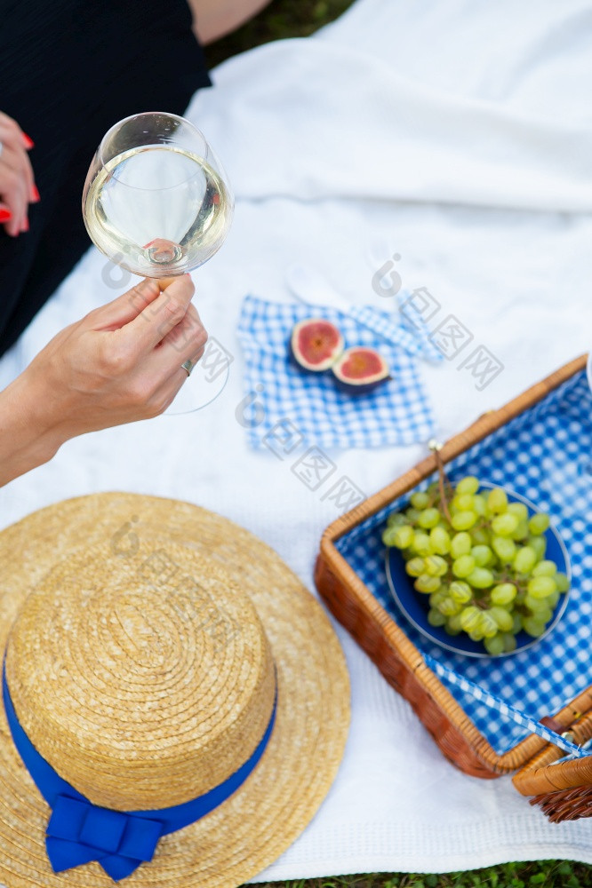 浪漫的野餐的公园的草美味的食物篮子酒葡萄无花果奶酪蓝色的网纹桌布两个眼镜酒的女孩持有玻璃酒她的手的概念户外娱乐浪漫的野餐的公园的草美味的食物篮子酒葡萄无花果奶酪蓝色的网纹桌布两个眼镜酒的女孩持有玻璃酒