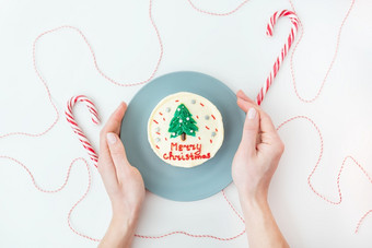 女孩持有板与圣诞节蛋糕与的登记快乐圣诞节装饰与糖衣白色背景与棒棒糖和红色的线程为礼物女孩持有板与圣诞节蛋糕与的登记快乐圣诞节装饰与糖衣白色背景与棒棒糖和红色的线程为礼物