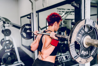 红色的头发女人做下蹲腿培训与杠铃的健身房回来视图健身健身