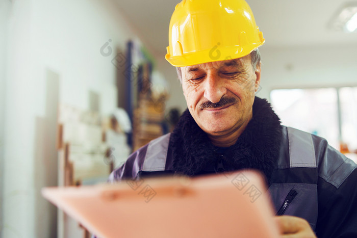 肖像高加索人高级男人。建设工人一般劳动者建筑承包商穿黄色的保护头盔持有笔和文档检查数据报告项目的办公室仓库