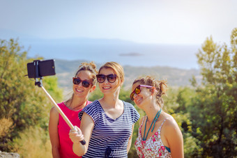 三个美丽的女孩女旅行者夏天礼服采取自拍与智能手机使用自拍坚持朋友友谊在户外的山以上的海秋天